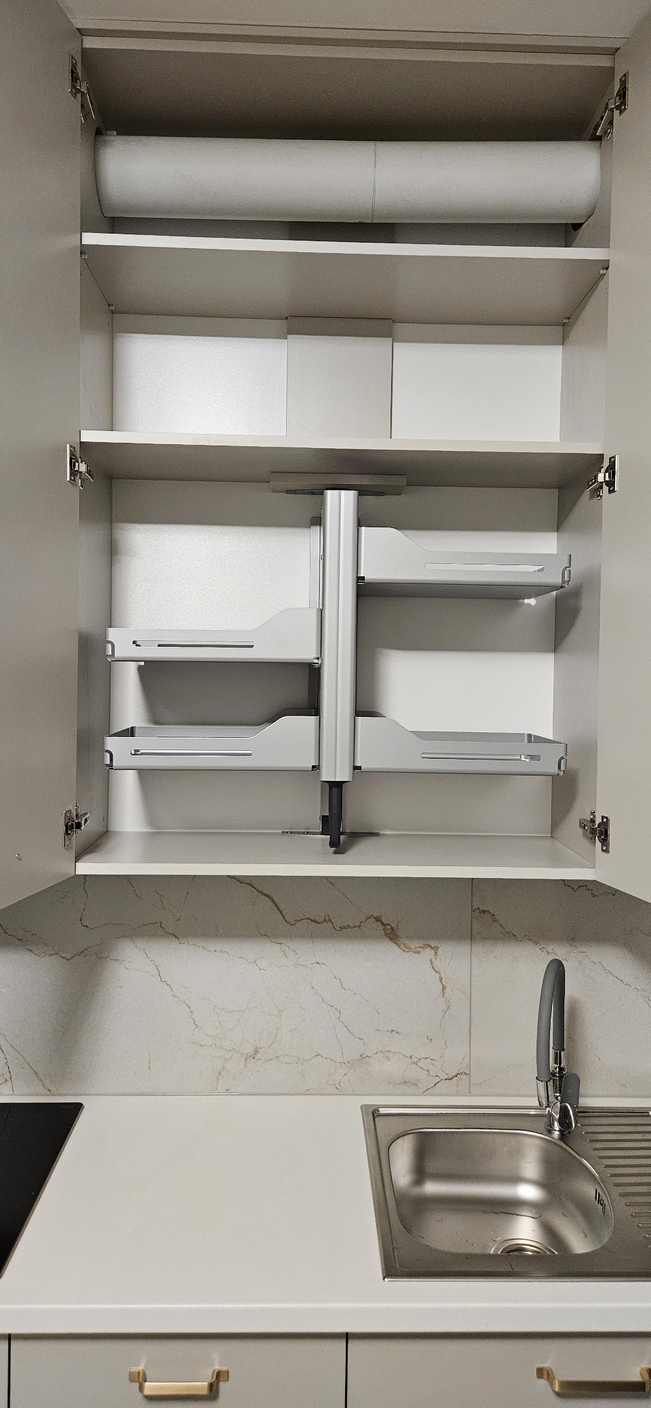 Wewnętrzny mechanizm obrotowy półek w szafce kuchennej, z widocznym zlewem i baterią na blacie.