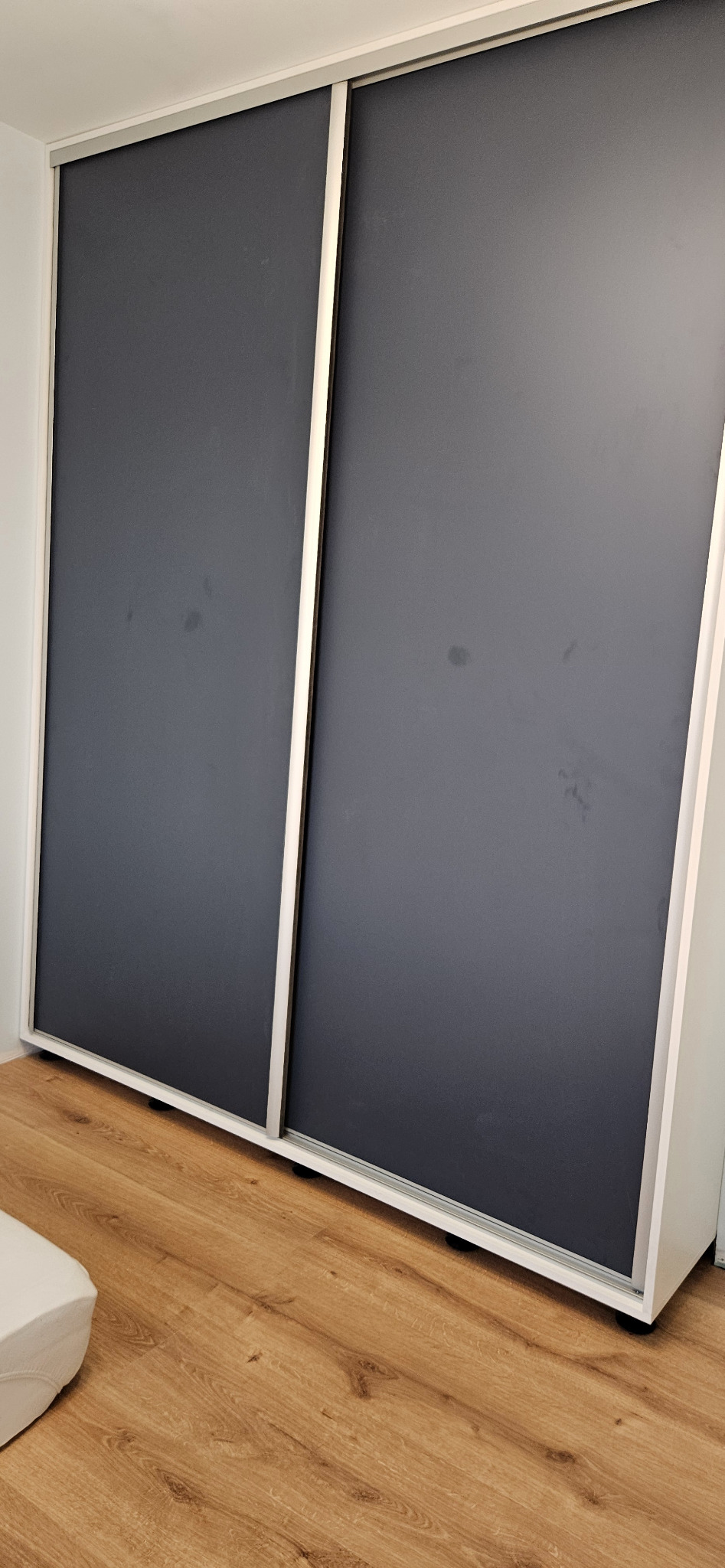 Szafa wnękowa z przesuwnymi drzwiami w kolorze grafitowym, białe obramowanie, widoczna podłoga z paneli imitujących drewno.