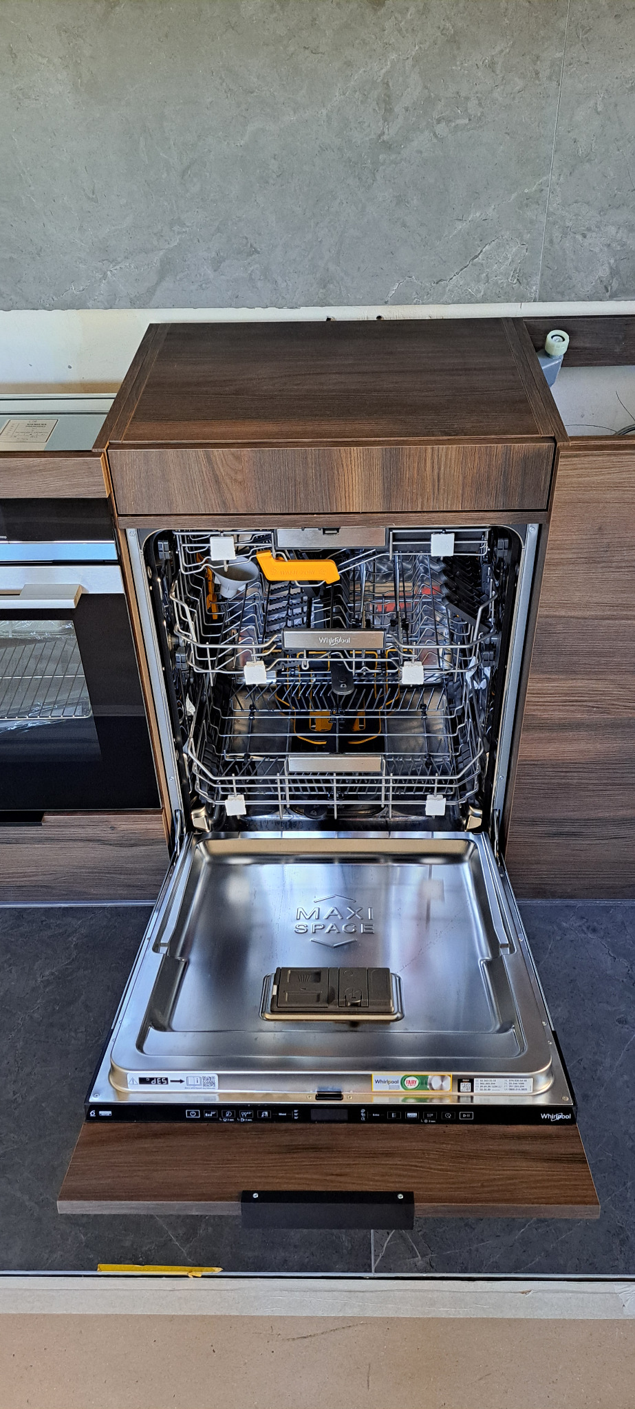 Otwarta zintegrowana z zabudową kuchenną zmywarka Whirlpool z widocznymi koszami i napisem MAXI SPACE na dnie.