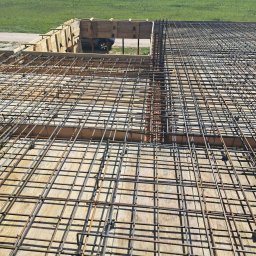 BOSS SYLWIA BOKSA - Zbrojenie płyty fundamentowej z deskowaniem, widok z góry na siatkę stalową i drewniane szalunki, w tle zielony teren z drzewami.