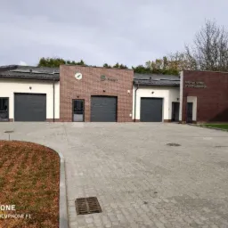 Nowoczesny budynek z garażami i elementami z czerwonej cegły, widok z zewnątrz na utwardzony plac.