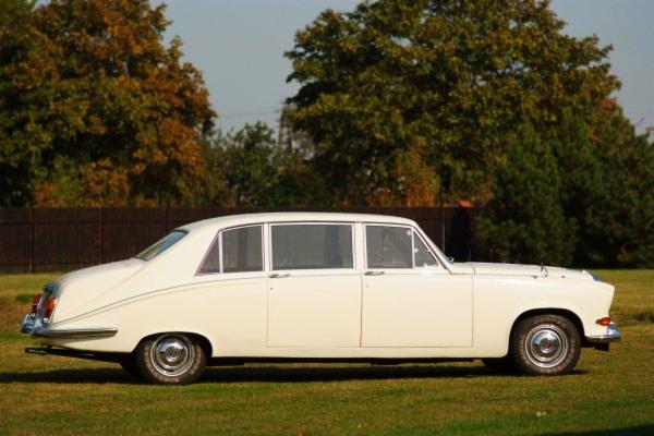 Elegancka, biała limuzyna z lat 70. na trawniku w Poznaniu. Auto po renowacji, z chromowanymi detalami, idealne na wyjątkowe okazje. Klasyczny styl i komfort.