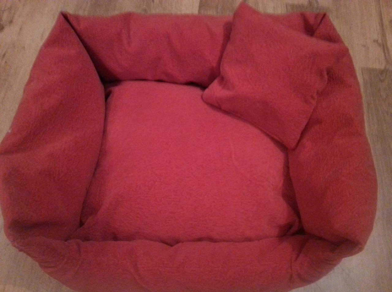 Różowe legowisko dla psa z poduszką, wykonane z miękkiego materiału. Widoczne szwy i faktura tkaniny. Produkt gotowy do użycia.