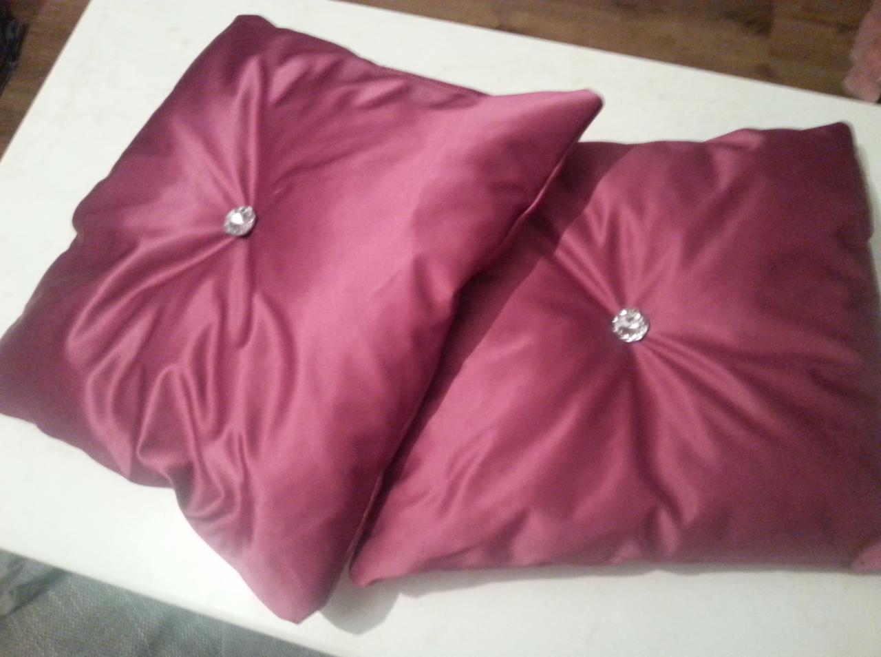 Dwie burgundowe poduszki dekoracyjne z błyszczącymi guzikami na białym tle, ukazujące eleganckie marszczenia materiału i staranne wykonanie.