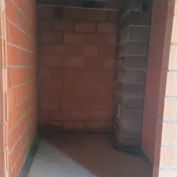 Surowy stan pomieszczenia z widocznymi ścianami z czerwonej cegły, fragmentem ściany z szarego bloczka i wylewką podłogową.