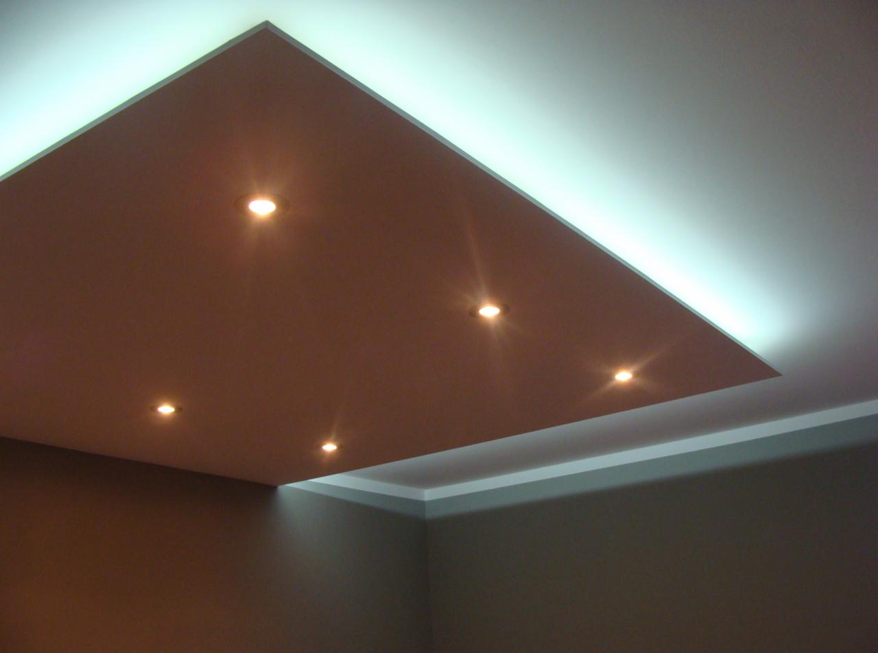 Kaskadowy sufit podwieszany w odcieniach brązu i bieli, oświetlony punktowymi lampami i listwą LED, tworzący nowoczesny design wnętrza.