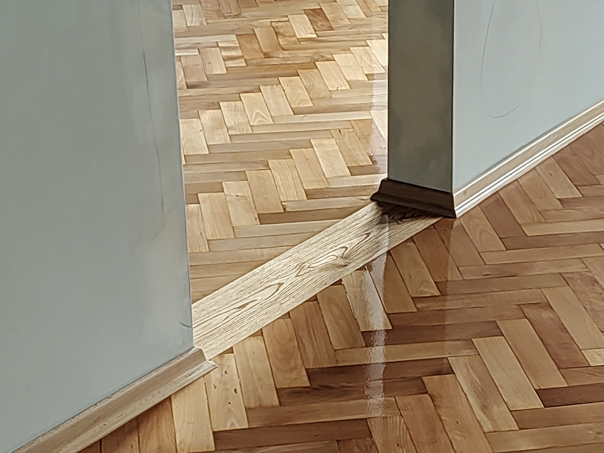 Parkiet ułożony w jodełkę, z widocznym przejściem przez próg drzwi, gdzie zastosowano jaśniejsze deski.