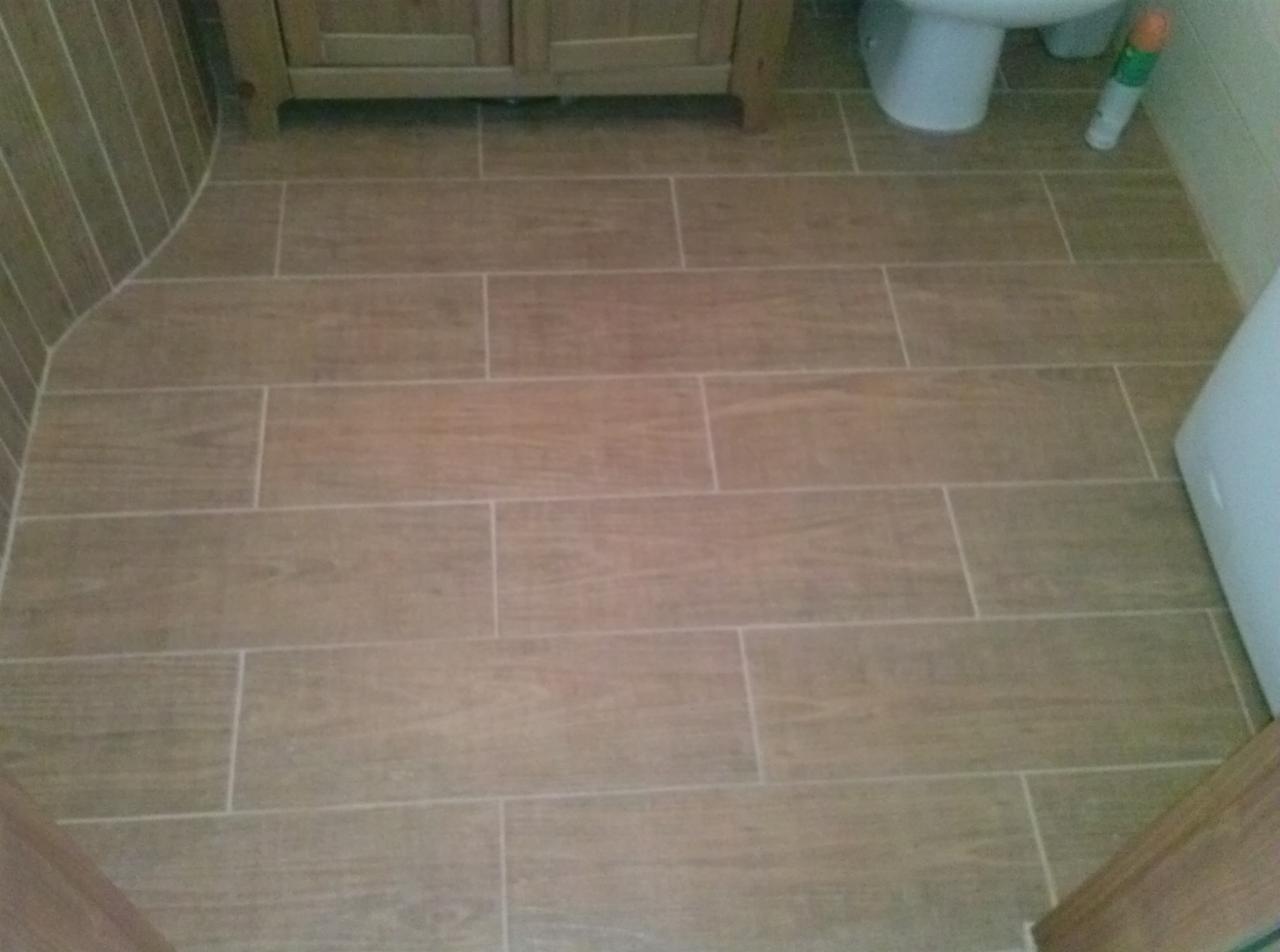 Ukończona podłoga w łazience wyłożona brązowymi płytkami imitującymi drewno, widoczna toaleta i fragment szafki pod umywalką.