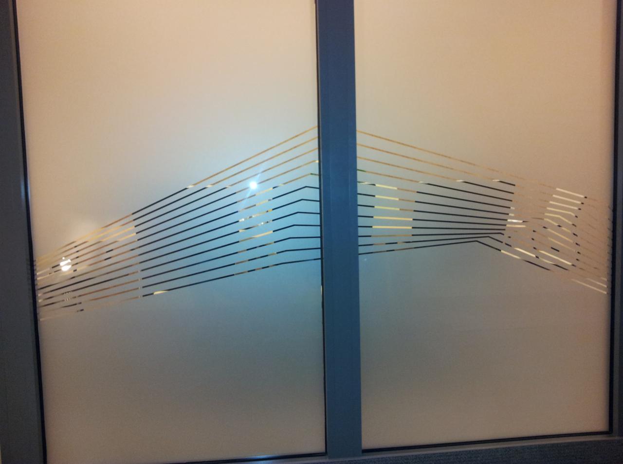 Matowe szkło okienne z dekoracyjnym wzorem z cienkich, poziomych linii w kolorze czarnym i złotym, tworzących abstrakcyjny motyw graficzny.