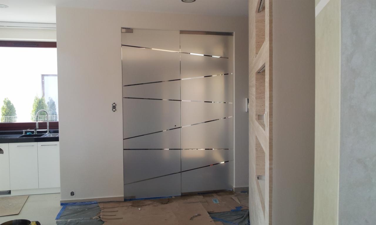 Matowe, przesuwne drzwi szklane z poziomymi paskami w nowoczesnym wnętrzu. Widoczna kuchnia w tle i elementy dekoracyjne ściany. Ochrona podłogi kartonem.