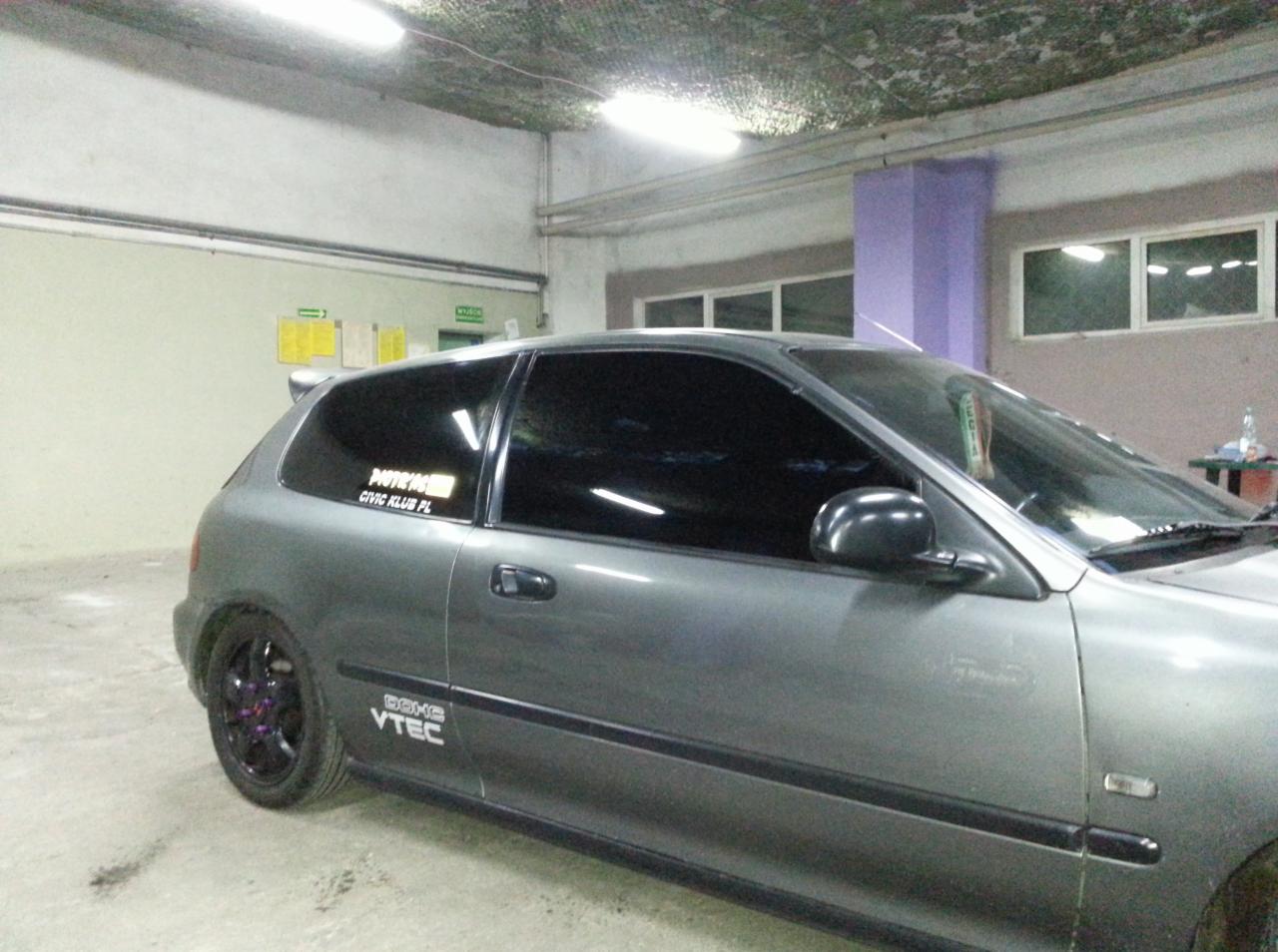 Szary hatchback z przyciemnionymi szybami, zaparkowany w warsztacie. Widoczne logo 'VTEC' i naklejka 'CIVIC KLUB PL'.