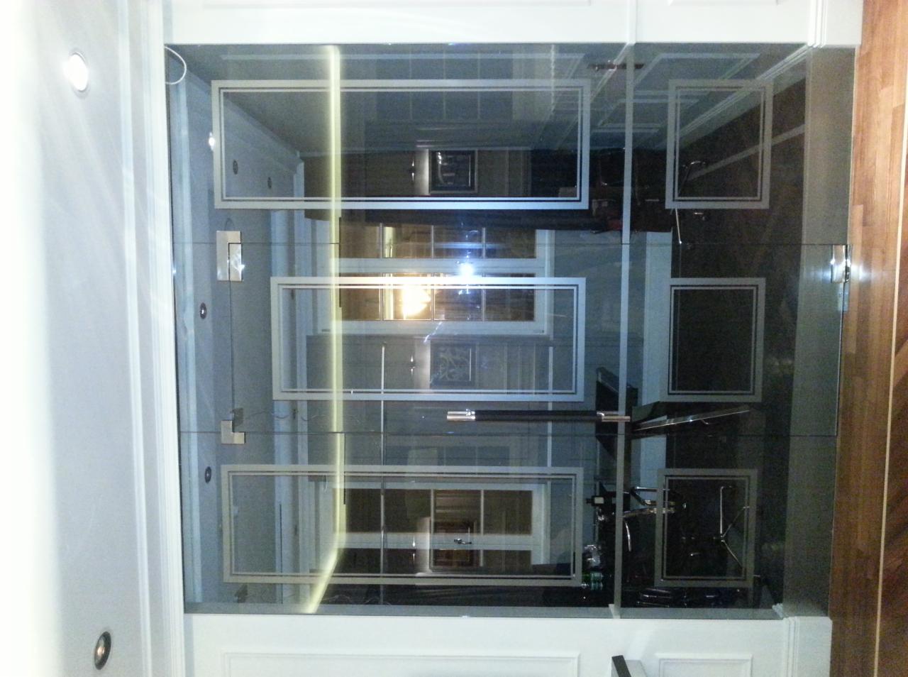 Szklana ściana działowa z dekoracyjnymi ramkami, oddzielająca przestrzeń w nowoczesnym wnętrzu. Widoczne elementy wyposażenia kuchni i salonu.