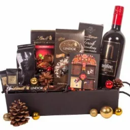 Czarny kosz z winem Neblina, czekoladami Lindt, kawą i dekoracjami świątecznymi, ustawiony na białym tle.