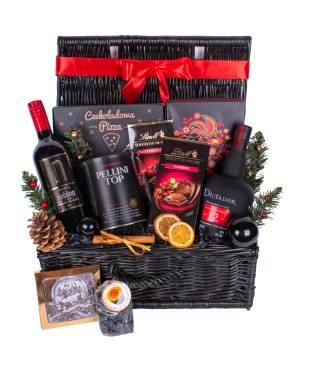 Czarny wiklinowy kosz wypełniony winem, likierem, kawą w puszce, czekoladą, piernikami, pomarańczami i dekoracjami świątecznymi, przewiązany czerwoną wstążką.