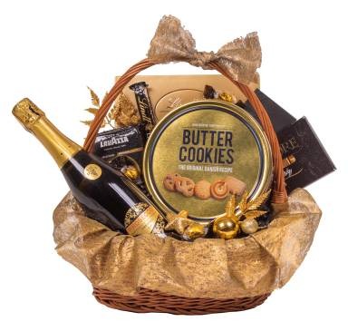 Wiklinowy kosz wypełniony szampanem w czarnej butelce ze złotą etykietą, puszką ciastek maślanych, kawą Lavazza i czekoladami, udekorowany złotymi ozdobami i kokardą.