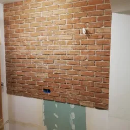 Fragment ściany w trakcie wykańczania z imitacją cegły w Jarocinie, widoczne puszki elektryczne i niedokończone dolne partie ściany.