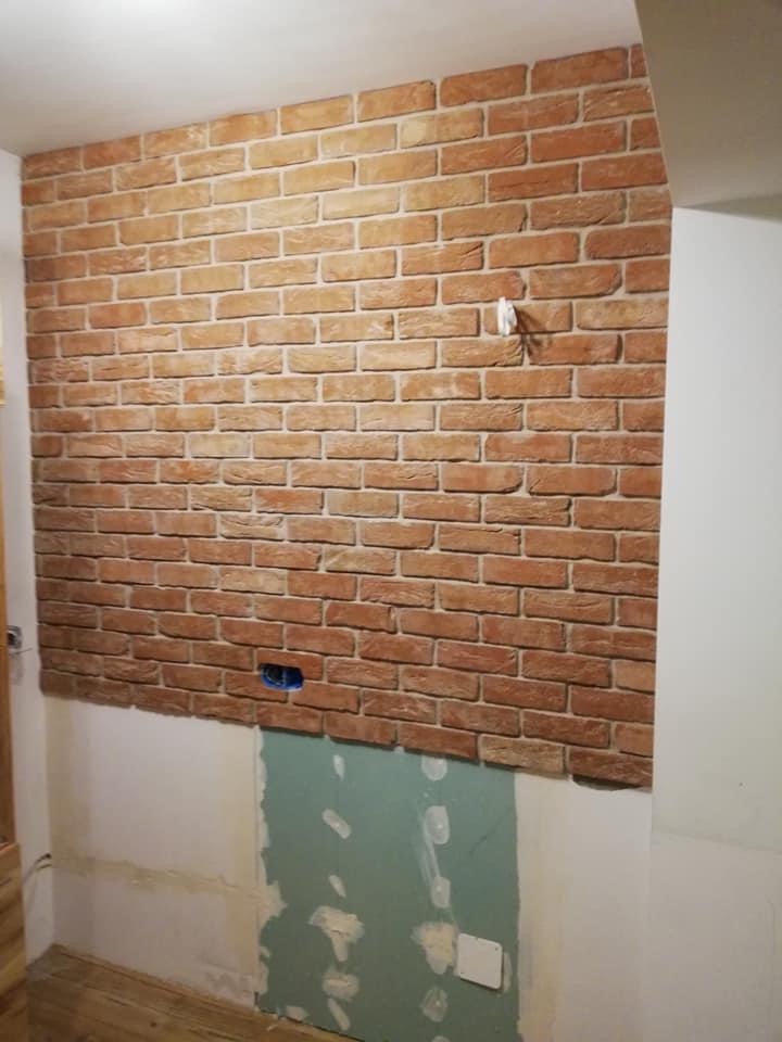 Fragment ściany w trakcie wykańczania z imitacją cegły w Jarocinie, widoczne puszki elektryczne i niedokończone dolne partie ściany.