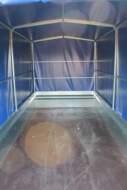 Wnętrze pustej, zadaszonej przyczepy transportowej z metalową konstrukcją i niebieskim brezentem, widoczne ślady użytkowania na podłodze.