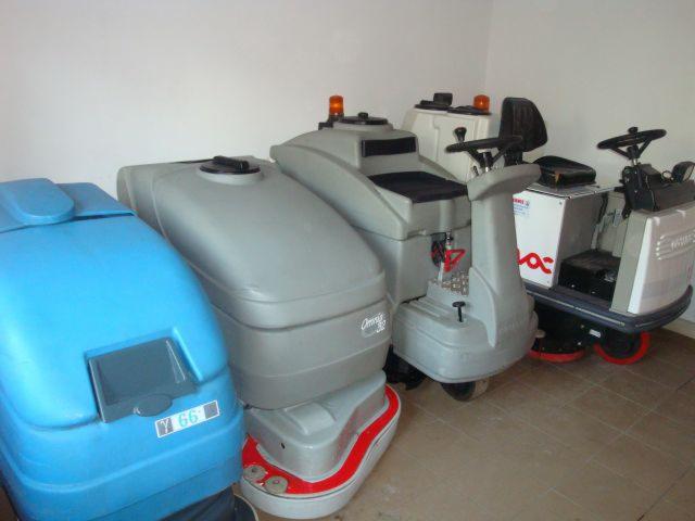 Różne modele automatów do mycia podłóg Comac, w tym Omnia 32b, ustawione obok siebie w pomieszczeniu, widoczne detale konstrukcyjne i kolorystyka.