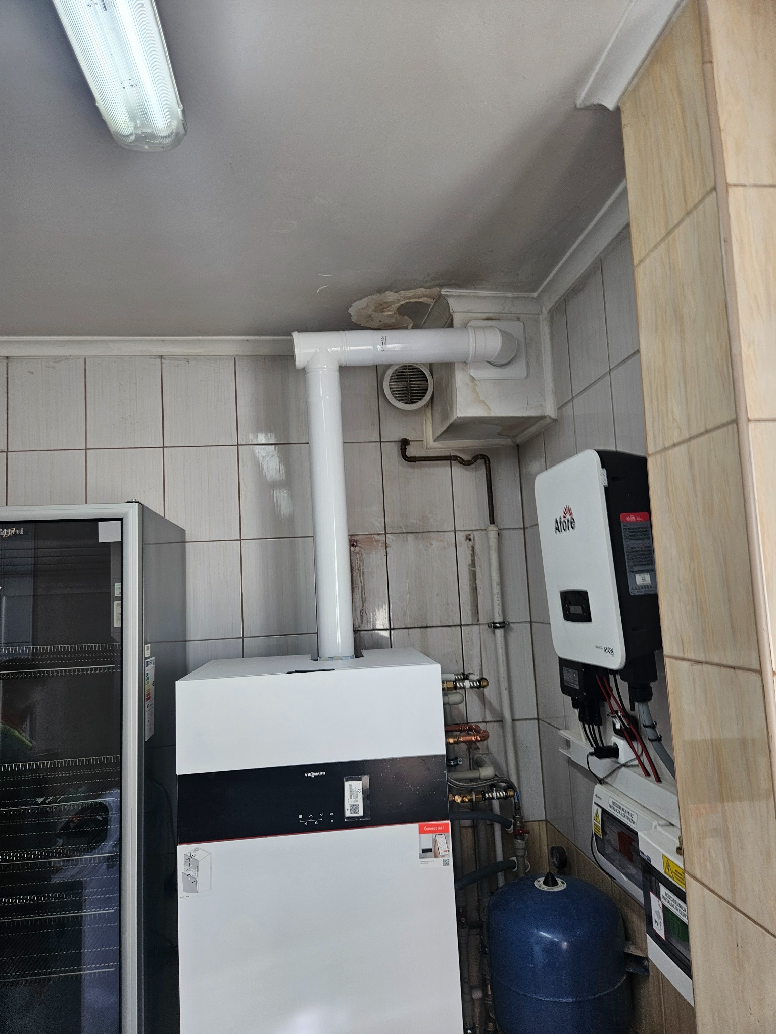 Biały piec Viessmann z podłączoną instalacją, widoczny zbiornik wyrównawczy i inwerter Afore na tle kafelkowanej ściany. Ujęcie w pomieszczeniu z oświetleniem jarzeniowym.