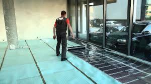 Montaż ogrzewania podłogowego: mężczyzna rozprowadza płyn na folii grzewczej w nowym budynku z dużymi oknami.