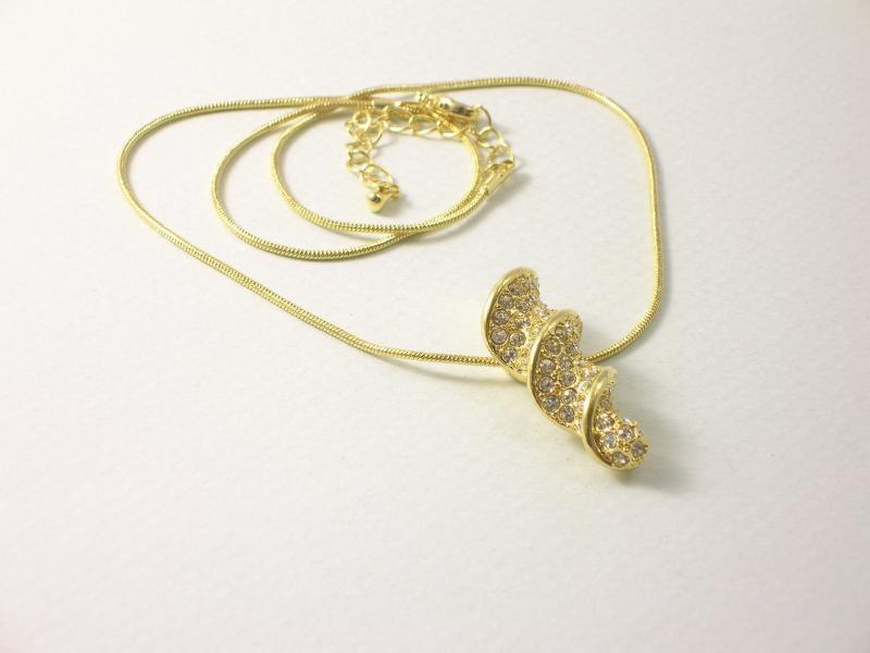 Złoty naszyjnik z błyszczącą, spiralną zawieszką na delikatnym łańcuszku, leżący na białym tle. Zawieszka ozdobiona drobnymi, połyskującymi kamieniami.