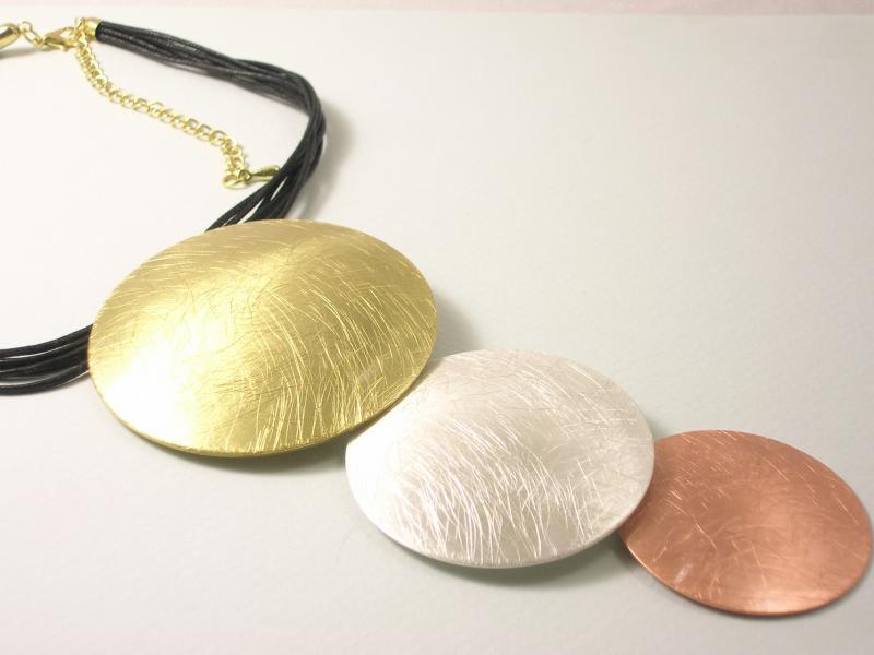 Naszyjnik z trzema okrągłymi zawieszkami w kolorach złota, srebra i miedzi, zawieszony na czarnych sznurkach z pozłacanym łańcuszkiem regulacyjnym.