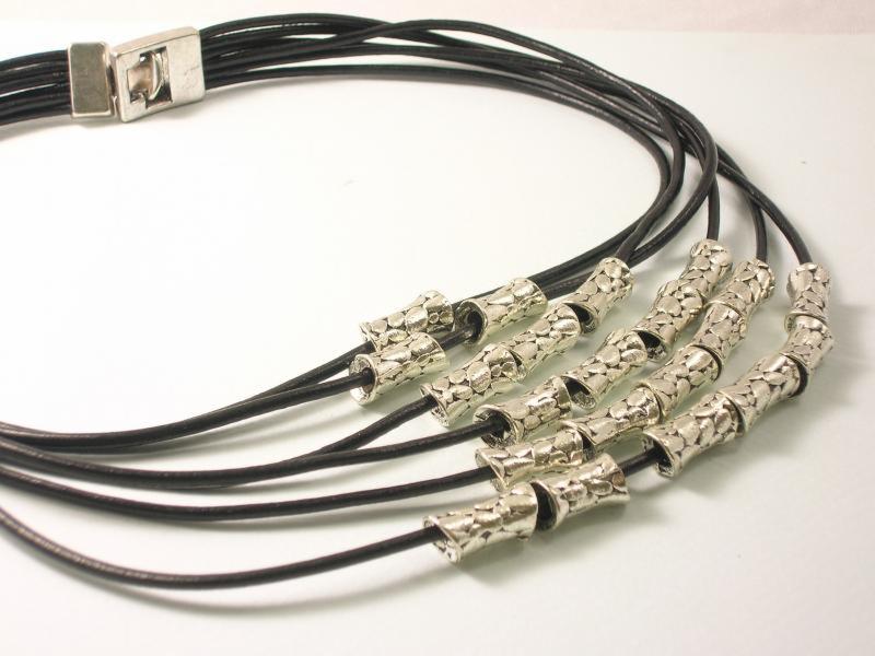 Czarny naszyjnik z pięcioma rzędami, srebrnymi zdobieniami i zapięciem. Delikatna biżuteria damska z bliska, na jasnym tle, z wyraźną fakturą elementów.