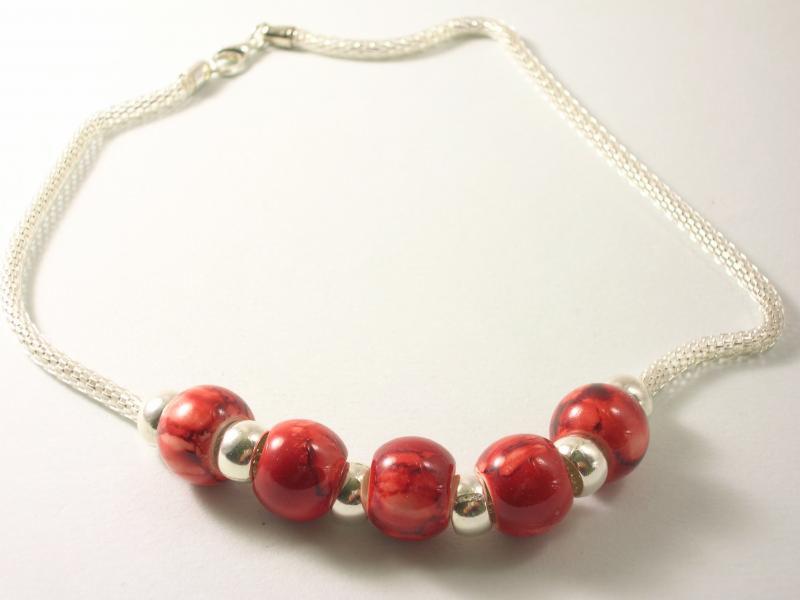 Delikatny srebrny łańcuszek z czerwonymi i srebrnymi koralikami na białym tle. Biżuteria damska, rękodzieło, unikalny wzór.