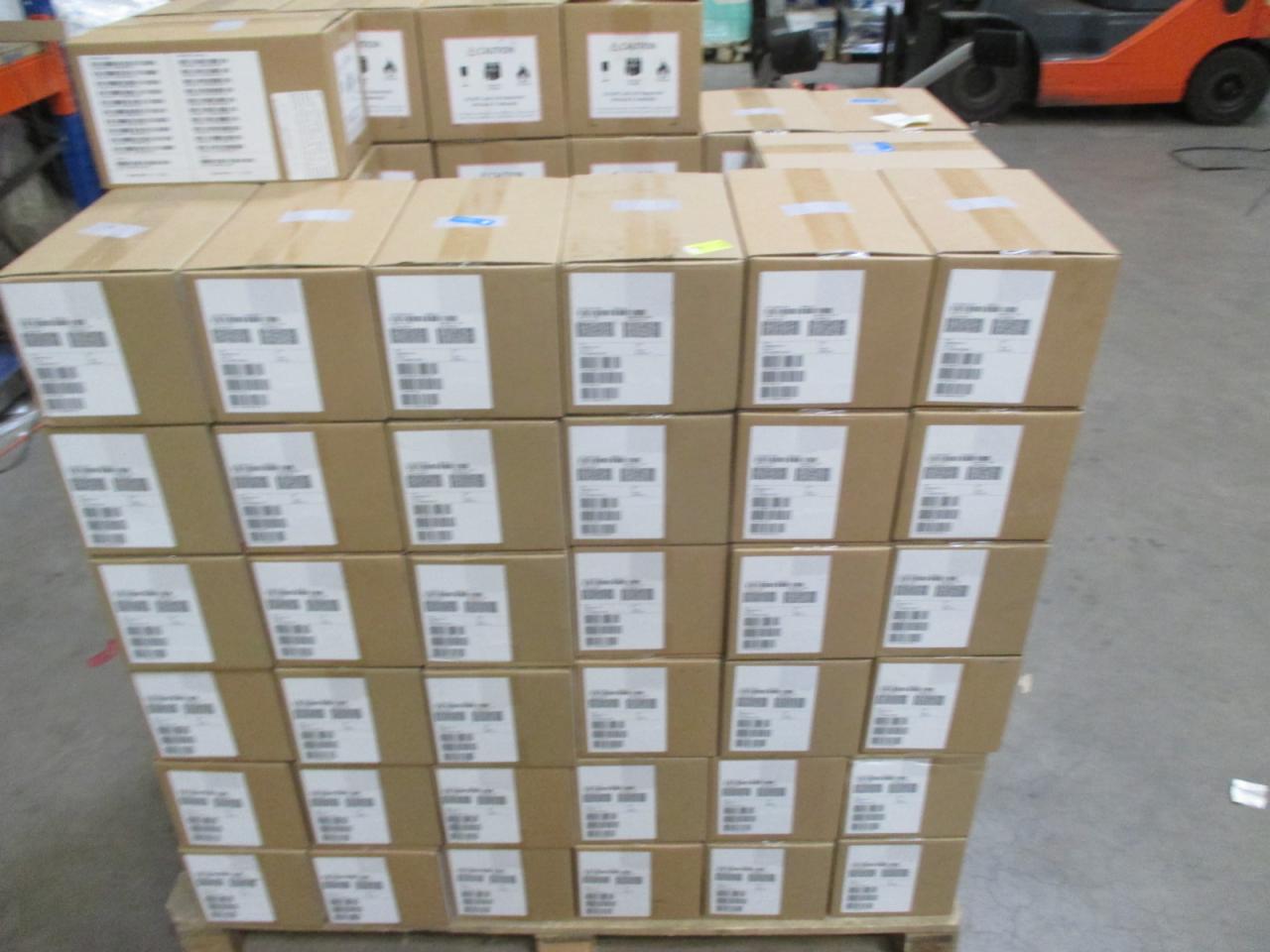 Paleta kartonów z naklejkami w magazynie, w tle wózek widłowy. Kartony ułożone jeden na drugim, tworząc stabilną konstrukcję. Widok z góry na paletę.