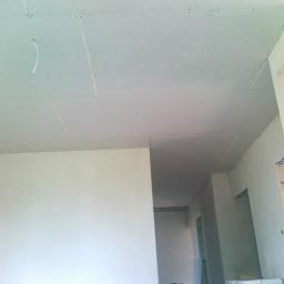 Brak - Sufit podwieszany z płyt gipsowo-kartonowych w trakcie montażu w Warszawie. Widoczne łączenia i śruby mocujące płyty. Świeżo wykończone ściany w tle.