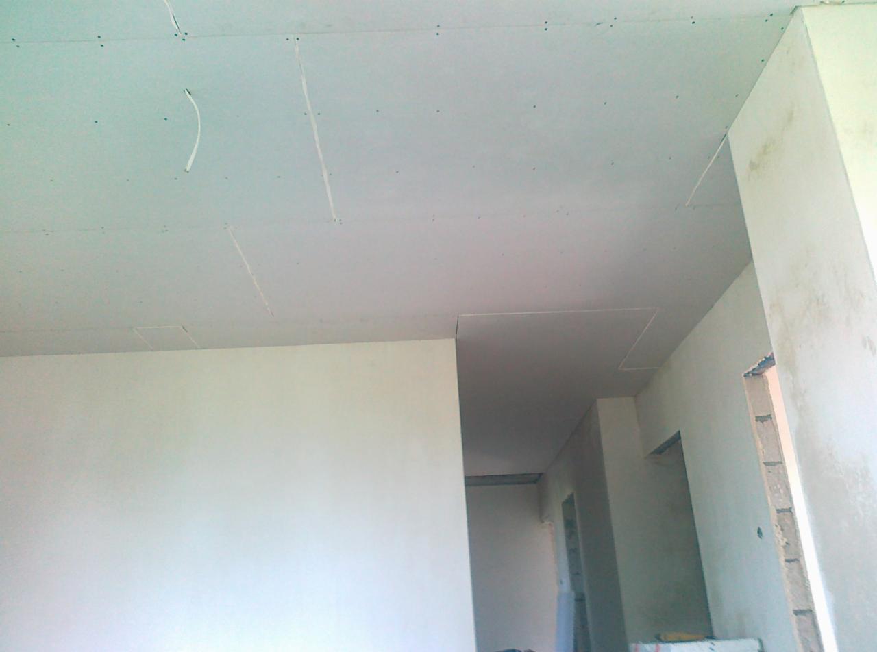 Sufit podwieszany z płyt gipsowo-kartonowych w trakcie montażu w Warszawie. Widoczne łączenia i śruby mocujące płyty. Świeżo wykończone ściany w tle.