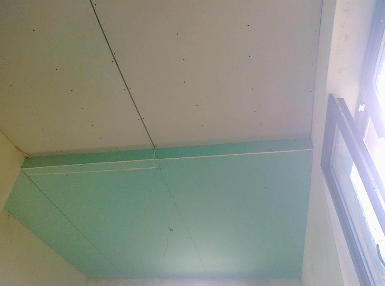 Montaż płyt kartonowo-gipsowych na suficie, widoczne łączenia i wkręty, fragment okna w prawym górnym rogu. Prace wykończeniowe w trakcie realizacji.