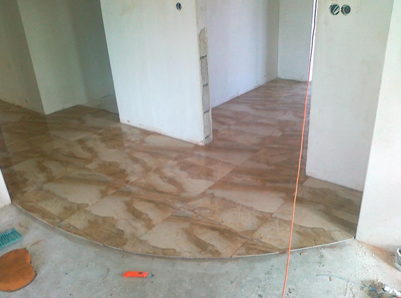 Wykończona podłoga z brązowych płytek w kształcie kwadratów, ułożonych w pomieszczeniu z białymi ścianami. Widoczny fragment pomieszczenia w trakcie remontu.