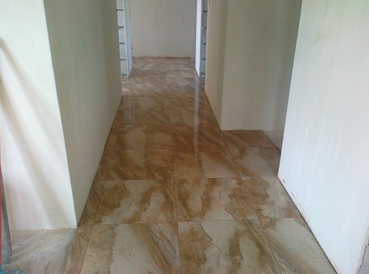 Ułożona, beżowo-brązowa terakota w korytarzu. Widoczne gładkie, białe ściany. W tle perspektywa kolejnych pomieszczeń z podobną posadzką.