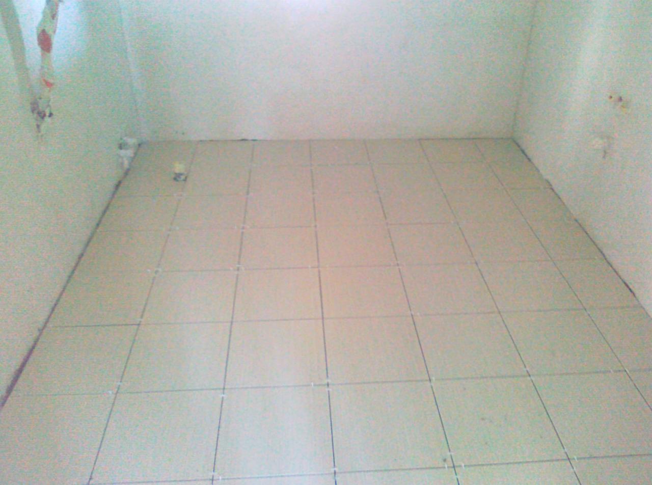 Ułożone, jasne płytki podłogowe w małym pomieszczeniu z surowymi ścianami. Widoczne krzyżyki dystansowe między płytkami.