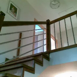 Drewniane schody z metalowymi poręczami, widok od dołu, na ścianie wiszą dwa zdjęcia w ramkach.