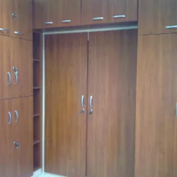 Zabudowa garderoby z drewnopodobnej płyty, widoczne drzwi przesuwne i półki boczne, srebrne uchwyty.