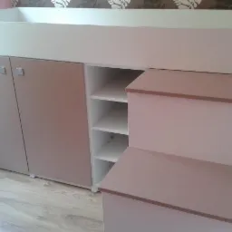 Wielofunkcyjna konstrukcja: podwyższone łóżko z szafkami i schodkami w odcieniach bieli i beżu, widoczne minimalistyczne uchwyty szafek i półki w otwartej części, na tle wzorzystej tapety.