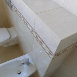 Nowo-Rem Piotr Nowosielski - Jasna łazienka z toaletą i bidetem. Płytki ceramiczne z motywem roślinnym zdobią ściany i obudowę stelaża podtynkowego. Ujęcie z góry, widoczne elementy armatury.