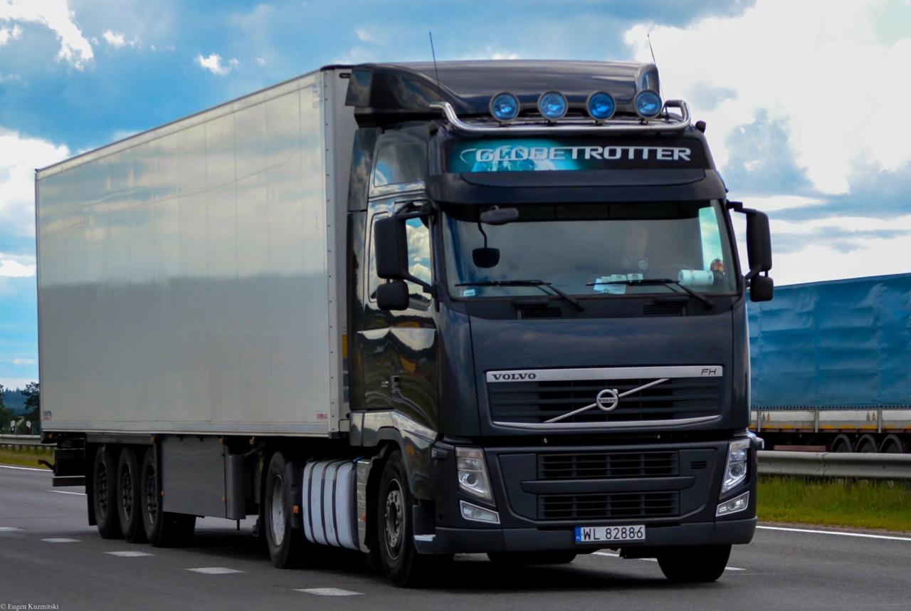 Czarny ciągnik siodłowy Volvo FH z naczepą chłodniczą na drodze, widoczne niebieskie światła obrysowe na dachu kabiny i napis 'Globetrotter'.
