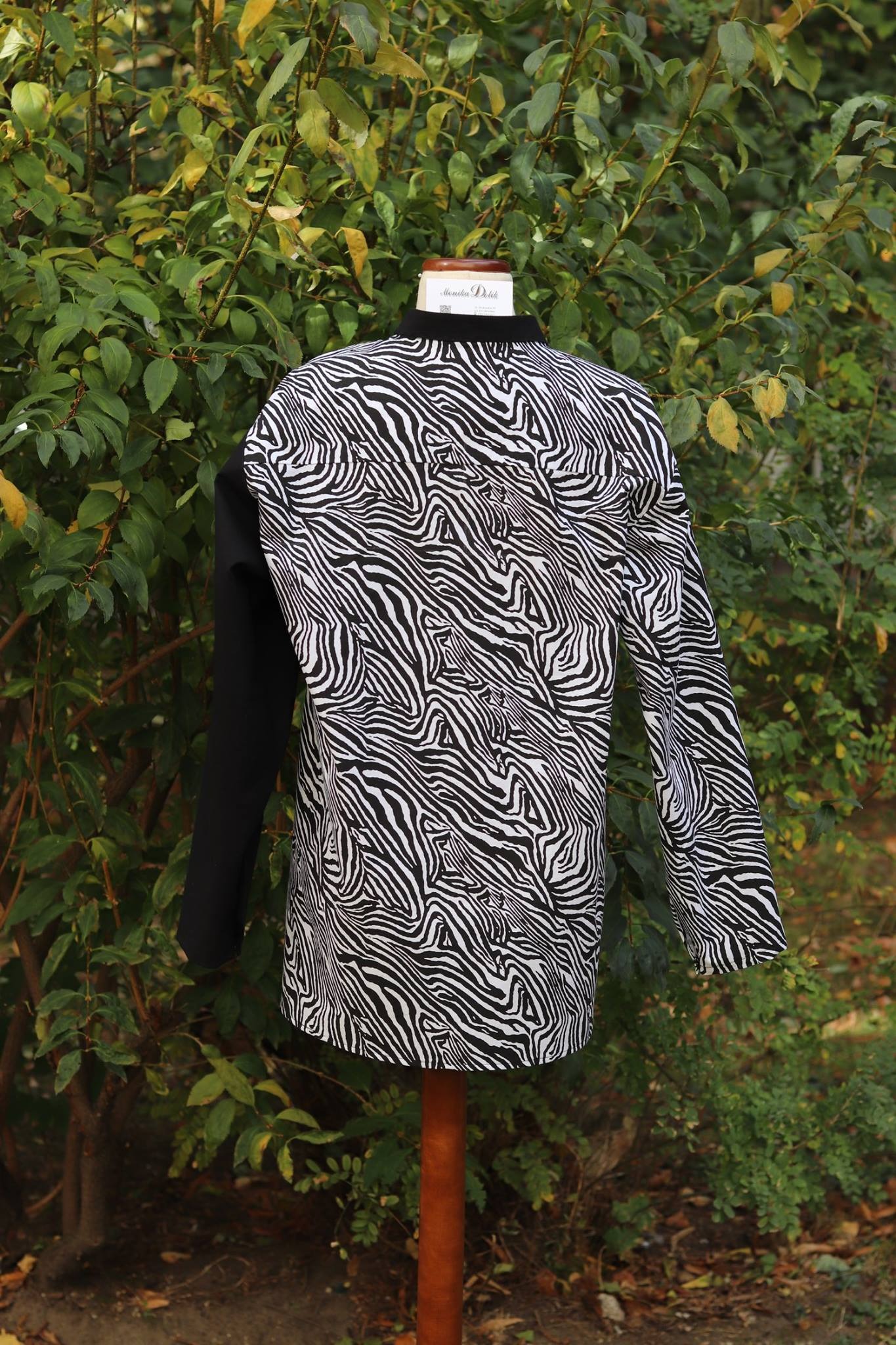 Czarno-biała kurtka w zebrę z jednym czarnym rękawem, na manekinie na tle zieleni, szycie na miarę we Wrocławiu. Nietypowy krój, unikalny wzór.