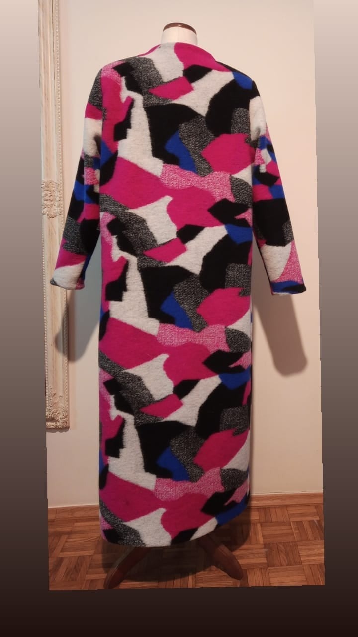 Długi, wełniany płaszcz na manekinie, wzór w nieregularne, kolorowe plamy (róż, biel, czerń, niebieski). Widok z tyłu, na jasnym tle.