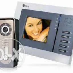 Zestaw wideodomofonowy: panel zewnętrzny z kamerą i monitor z wizerunkiem kobiety, widoczne przyciski sterujące i głośnik. Nowoczesny design, srebrno-szara kolorystyka.