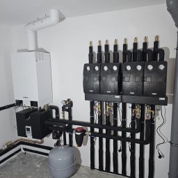 PHU VERSO ROBERT SERAFIN - Nowoczesna kotłownia gazowa z białym piecem Viessmann, czarnymi rurami i czterema czarnymi modułami sterującymi na białej ścianie. Szara podłoga i rura odpływowa.