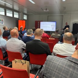 PHU VERSO ROBERT SERAFIN - Szkolenie Viessmann: grupa instalatorów siedzi na czerwonych krzesłach, słuchając prezentacji o marketingu na ekranie. Widoczny prelegent i logo Viessmann.