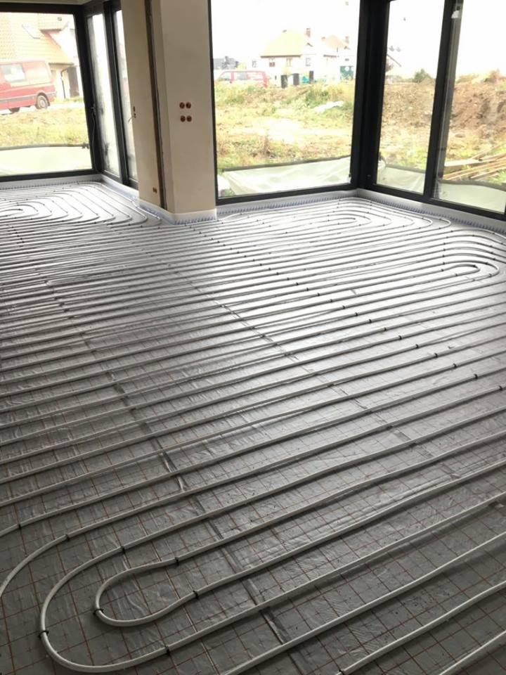 Równomiernie rozłożone rury ogrzewania podłogowego na folii izolacyjnej w przestronnym, jasnym pomieszczeniu z dużymi oknami.