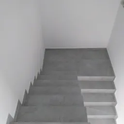 Schody wyłożone szarymi płytkami imitującymi marmur, widok z góry, białe ściany.