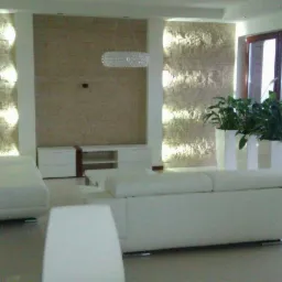 Elegancki salon z białymi meblami, ścianą z kamienia dekoracyjnego z podświetleniem, kryształowym żyrandolem i roślinami w białych donicach.