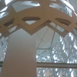 Ażurowa konstrukcja stalowa w budynku w Warszawie, widok z dołu ukazuje geometryczny wzór wycięty w metalu i jasne wnętrze hali.